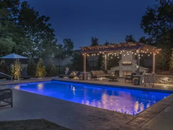 pool-at-night-hardscapes-1-scaled Backyard pool, pergola, and stone fireplace outdoor living space at night — Apex Landscaping