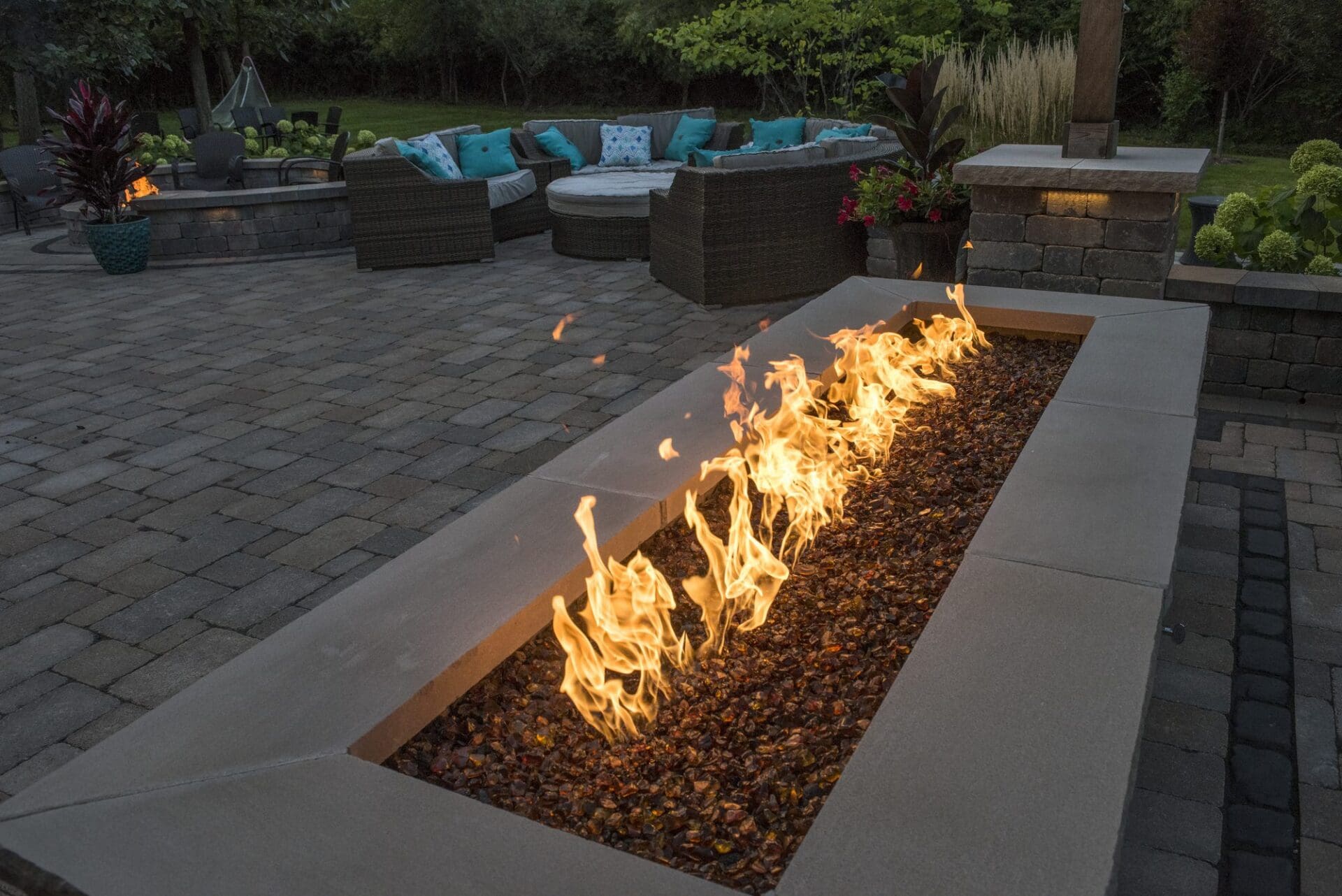 Long linear gas fire feature on a patio at dusk — Apex Landscaping outdoor living