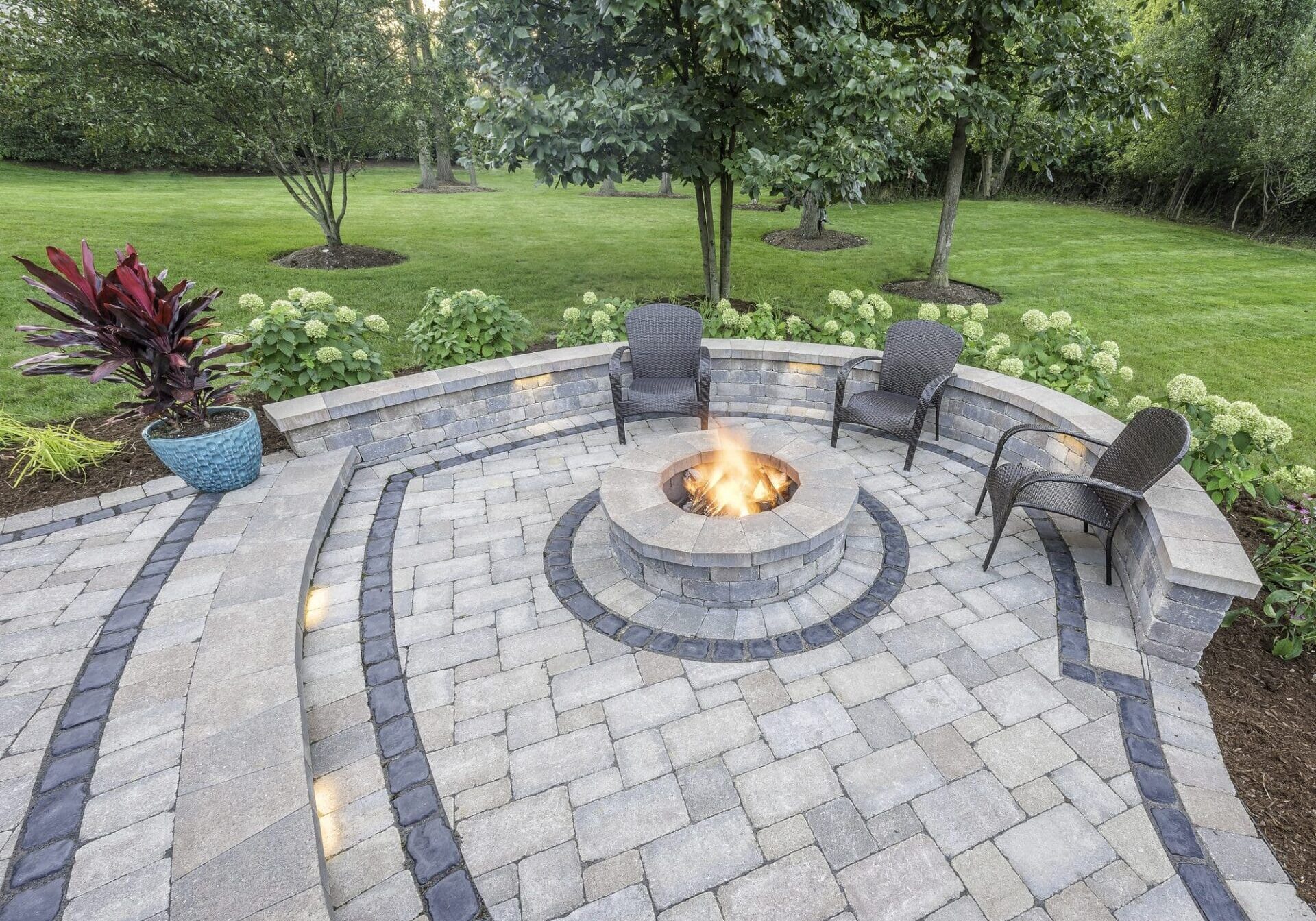 Circular paver fire-pit patio surrounded by garden plantings — Apex Landscaping